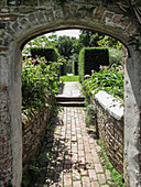 Blick durch gemauerten Rundbogen in Garten mit Hochbeet und Hecken