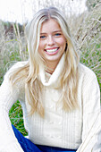 Junge blonde Frau in weißem Rollkragenpullover in der Natur
