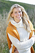 Young blond woman in white turtleneck sweater, with yellow knitted sweater slung over shoulders in nature
