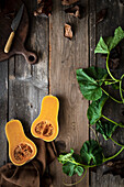 Halbierter Butternusskürbis mit Messer und Blättern auf rustikalem Holzuntergrund