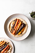 Honey roasted carrots with hummus and thyme in a ceramic bowl.