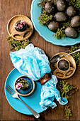 Easter table setting with empty turquoise ceramic plates and egg cups, decorated by forest moss, black colored easter eggs and pink spring flowers