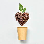 White coffee cup and coffee beans in shape of heart on white background, top view