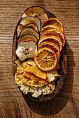 Thin slices of dried fruit, pineapple, apple and orange, on a small wooden tray, on a wooden table