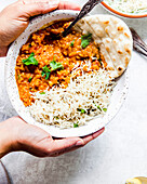 Lady holding a bowl of dal served with rice and naan bread