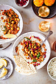 Two bowls of chickpea curry served with rice, lemon wedges, naan bread and garnished with pomegranate.