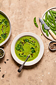 Green pea soup in a bowl, with sugarsnap peas and seasoning.