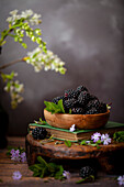 A wooden bowl filled with fresh blackberries with mint leaf garnish