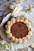 Overhead view of a chocolate cake decorated with whipped cream, chocolate flakes and cocoa powder