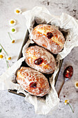 Three jam doughnuts dusted in sugar presented in a baking tin