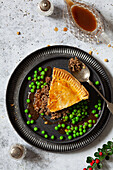 A slice of minced beef and onion pie with peas and gravy