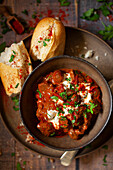 A bowl of beef goulash topped with soured cream and parsley with a side of cursty bread