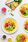 Tortillas with sliced avocados and chickpeas and lime slices and green pepper on white background