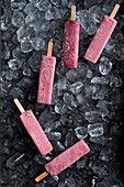 Yummy fruit ice pops placed on heap of ice cubes in fridge