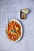 Tasty conchiglie pasta with tomato sauce and lemons and can of sardines on gray table