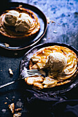 Apple tart with balls of ice cream served on plates with fork on dark marble table