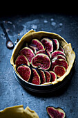 Baking pan with raw dough and slices of figs placed on dark gray table