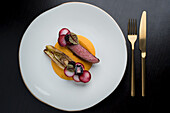 Appetizing beef with sweet potato puree served with tasty artichoke on white plate on black background