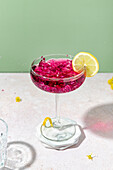 Transparent elegant glass filled with blackberry liqueur with ice and lemon slice on rim placed on table in studio