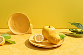 Fresh whole and halved sour lemons near apple on vivid ceramic plate on table on yellow background