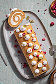 Sweet biscuit roll with cream filling served with dried berries and leaves on plate