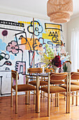 Dining area with glass table and vintage chairs behind modern artwork on concrete slab