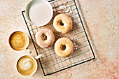 Glazed donuts on a cooling rack next to two cups of coffee