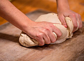 Hands kneading raw soft dough on cutting board while preparing for baking bread