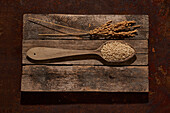 Wooden spoon with raw sesame seeds on wooden boards with rice ears placed on table in light room
