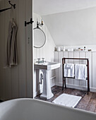 Freestanding bath in attic bathroom with repurposed paneling on the wall and pedestal sink