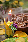 Glas mit Kerze und Blumen als Tischdekoration