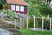 Eingezäuntes Sommerbeet im Garten in Hanglage, im Hintergrund rot-braunes Holzhaus