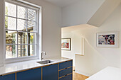 Blaue Küchenzeile unterm Sprossenfenster und verwinkelter Durchgang