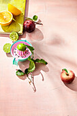 A citrus press with citrus fruits, red plums and peaches on pink surface