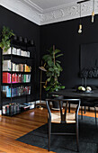 Bücherregal und Zimmerpflanze vor schwarzer Wand in Zimmerecke