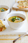Vegan coconut and lentil curry soup topped with toasted coconut and coriander leaves alongside garlic naan bread