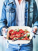 Roasted stuffed peppers in enamel dish held by person in denim clothing