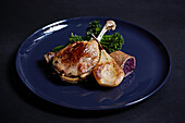 Duck leg served with pear on a blue plate