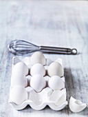 White eggs in an egg crate with a whisk behind it