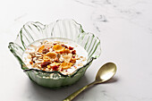 Bowl with yogurt and breakfast cereals next to a metal spoon on a table