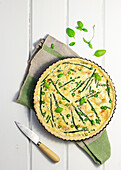 Top view of yummy asparagus quiche with basil leaves placed on wooden table