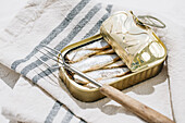 Top view of a can of sardines open in half on a tablecloth on white background