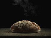 Delicious freshly baked sourdough bread loaf with crispy crust covered with flour placed on table against black background in kitchen