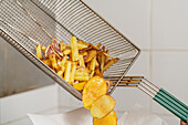 Pommes Frites und Chips aus einem Frittierkorb in eine Schüssel geben