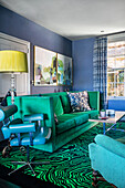 Grünes Sofa, Vintage Lederstuhl und Teppich mit Malachitmuster im Wohnzimmer mit blauen Wänden