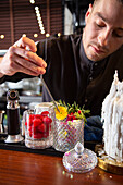 Serious barkeeper in black uniform decorating cocktail with fresh flower during work in bar