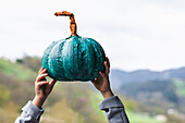 Unrecognizable cropped girl with teal pumpkin standing in rural area with mountains on blurred background