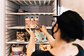 Frau stellt dekorative Torte in den Kühlschrank einer Konditorei