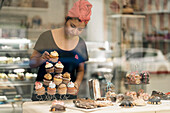 Frau mit Kopftuch richtet Cupcakes in einer Konditorei an
