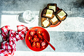 From above summer salad of ripe red cherry tomatoes in the bowl and toasts with melted cheese on concrete background